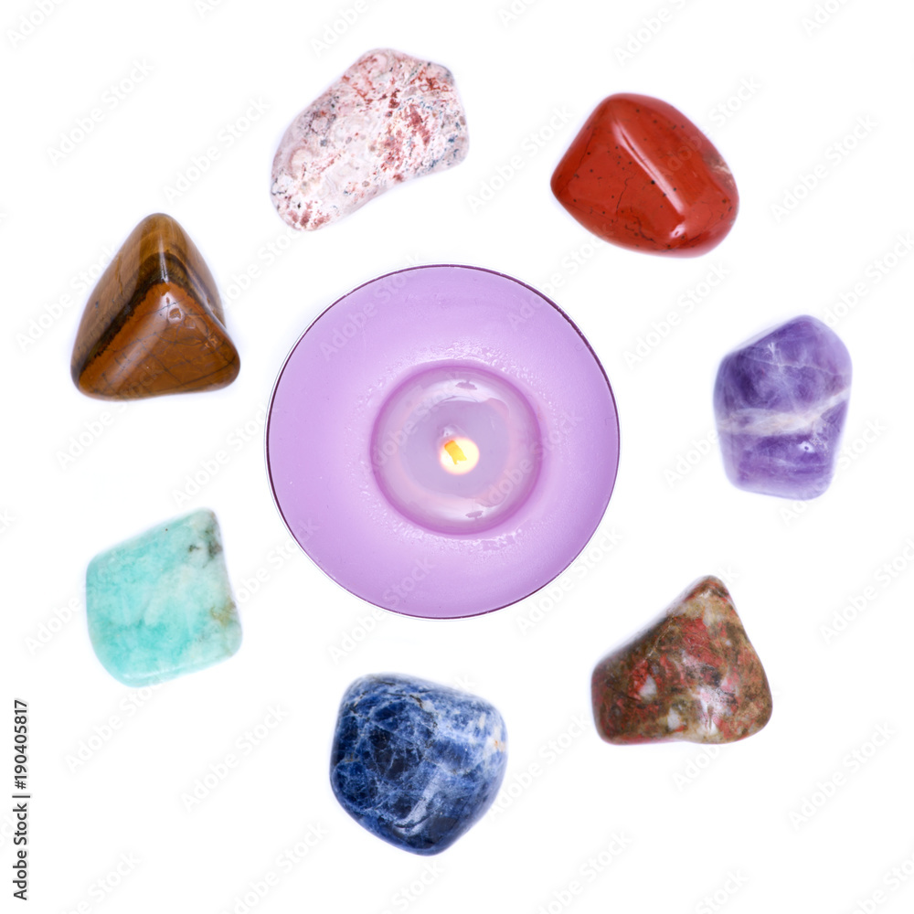 Lavender tea light candle surrounded by set of seven healing chakra stones for crystal healing, isolated on white background Lavender tea light candle surrounded by set of seven healing chakra stones for crystal healing, isolated on white background