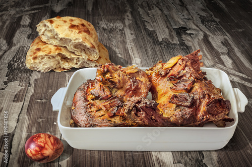 Freshly Oven Baked Lamb Shoulder In Porcelain Casserole Served With Leavened Pitta Flatbread And Decorated Red Dyed Easter Egg On Old Lacquered Cracked Flaky Garden Table