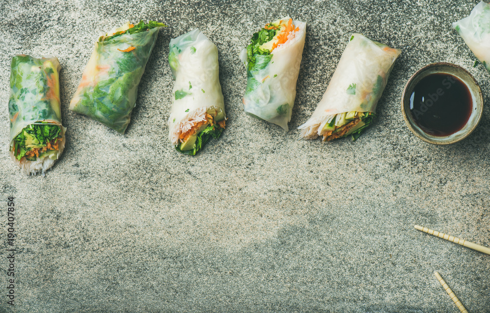 Helathy Asian cuisine. Flat-lay of vegan spring or summer rice paper rolls with vegetables, sauce and chopsticks over concrete background, top view, copy space. Clean eating, vegetarian, dieting food