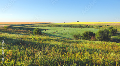 Sunny summer landscape.Green meadows,fields and straw bales at sunrise 
