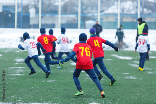 Young kids football tournament - children play match on soccer field during the snow falling