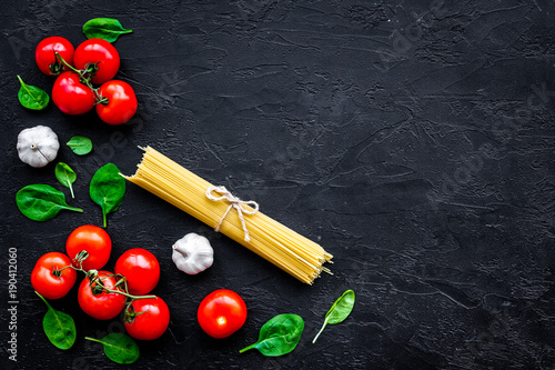 Cook spaghetti with tomatoes, garlic, basil. Italian recipe. Black wooden background top view copy space