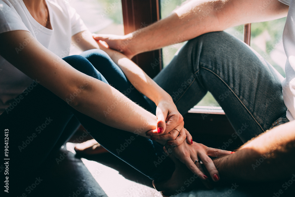 Fototapeta premium The guy and the girl are sitting together by the window, Hands and feet of a guy and a girl.