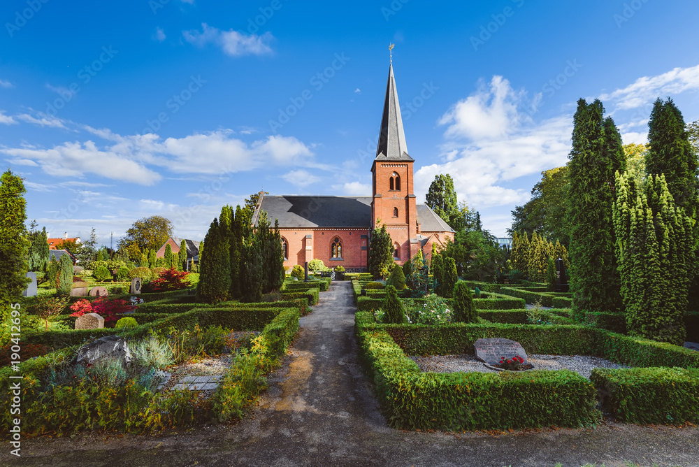 Old city cemetary and catholic church in Dragor, Denmark - September, 21th, 2015. Gravestones, greenery and cloud sky at the early morning in fishman village near Copenhagen.
