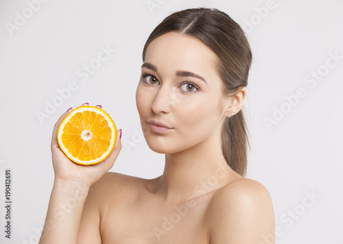 Beautiful brunette holding an orange with a stunning look on a white background  photo