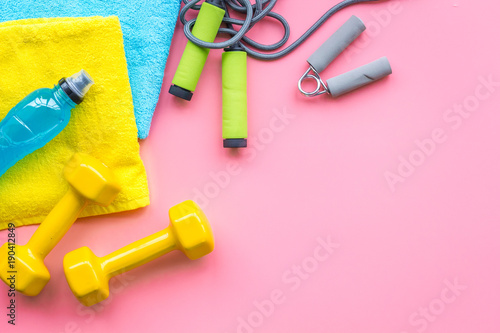 Fitness background. Equipment for gym and home. Jump rope, dumbbells, expander, mat, water on pastel pink background top view copy space