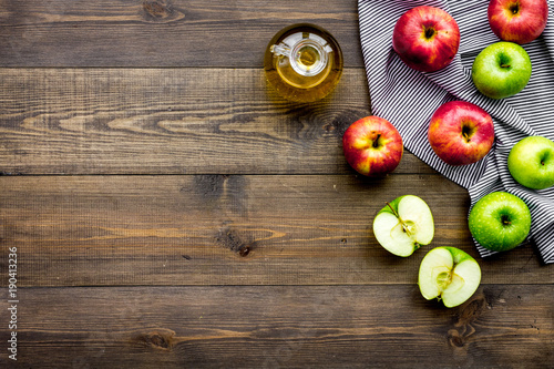 Light salad dressing. Apple cider vinegar in bottle among fresh apples on dark wooden background top view copy space