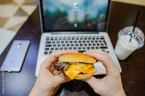 man eat burger in cafe and work on laptop photo