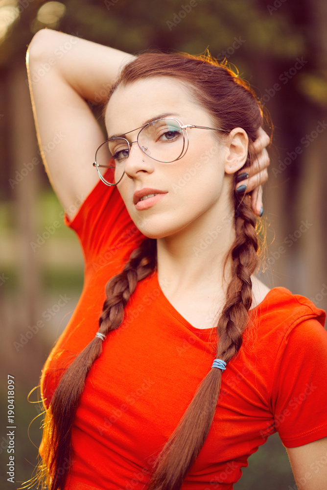 Young beautiful sexy woman in red virgin pigtail glasses blue shorts white  summer sneakers in the park. Close portrait Stock-bilde | Adobe Stock