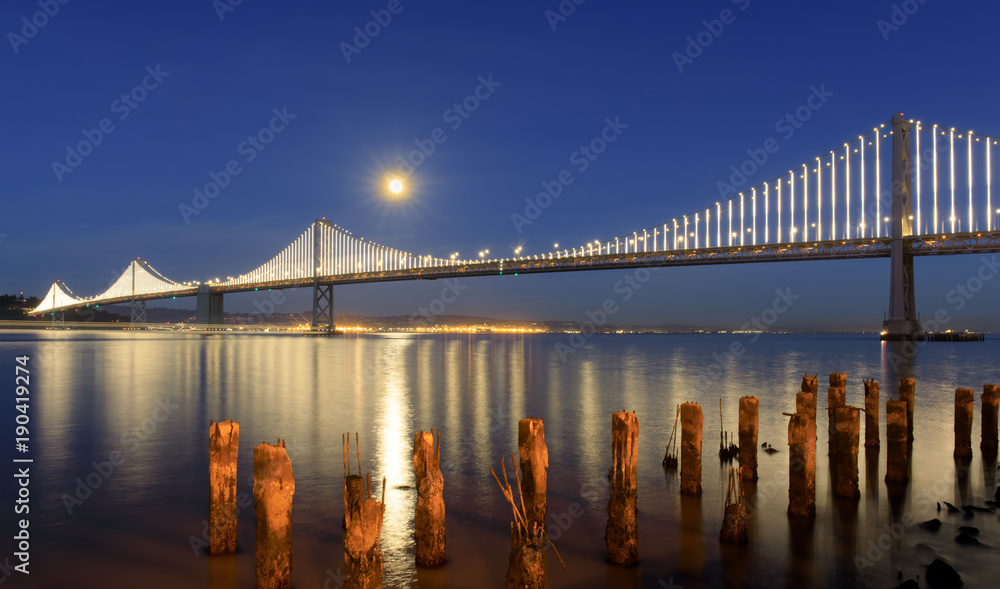 San Francisco-Oakland Bay Bridge with full moon rising at dusk. The Embarcadero, San Francisco, California, USA.