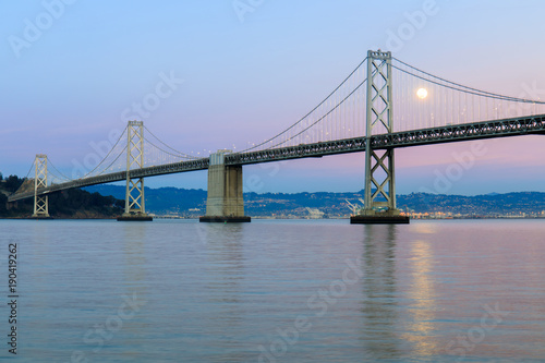 San Francisco-Oakland Bay Bridge with full moon rising and pink and blue sunset skies. The Embarcadero, San Francisco, California, USA. #190419262