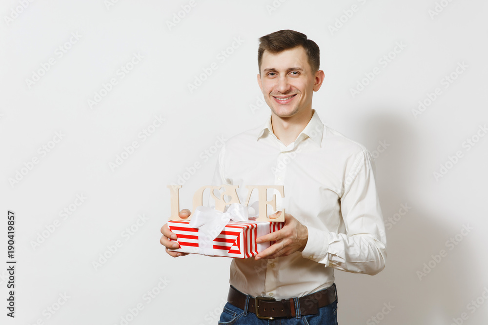 Young smiling man holding wooden word Love, red present box with gift isolated on white background. Copy space advertisement. St. Valentine's Day, International Women's Day, birthday, holiday concept. Young smiling man holding wooden word Love, red present box with gift isolated on white background. Copy space advertisement. St. Valentine's Day, International Women's Day, birthday, holiday concept.