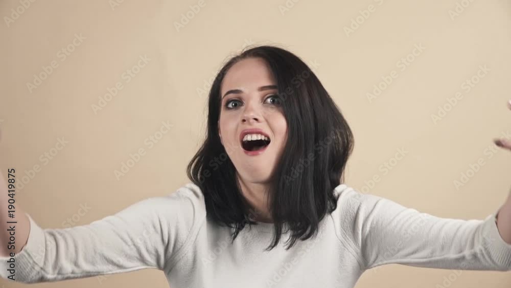 a young beautiful cute brunette on a beige orange background showing fool, dances, laugh emotions a young beautiful cute brunette on a beige orange background showing fool, dances, laugh emotions