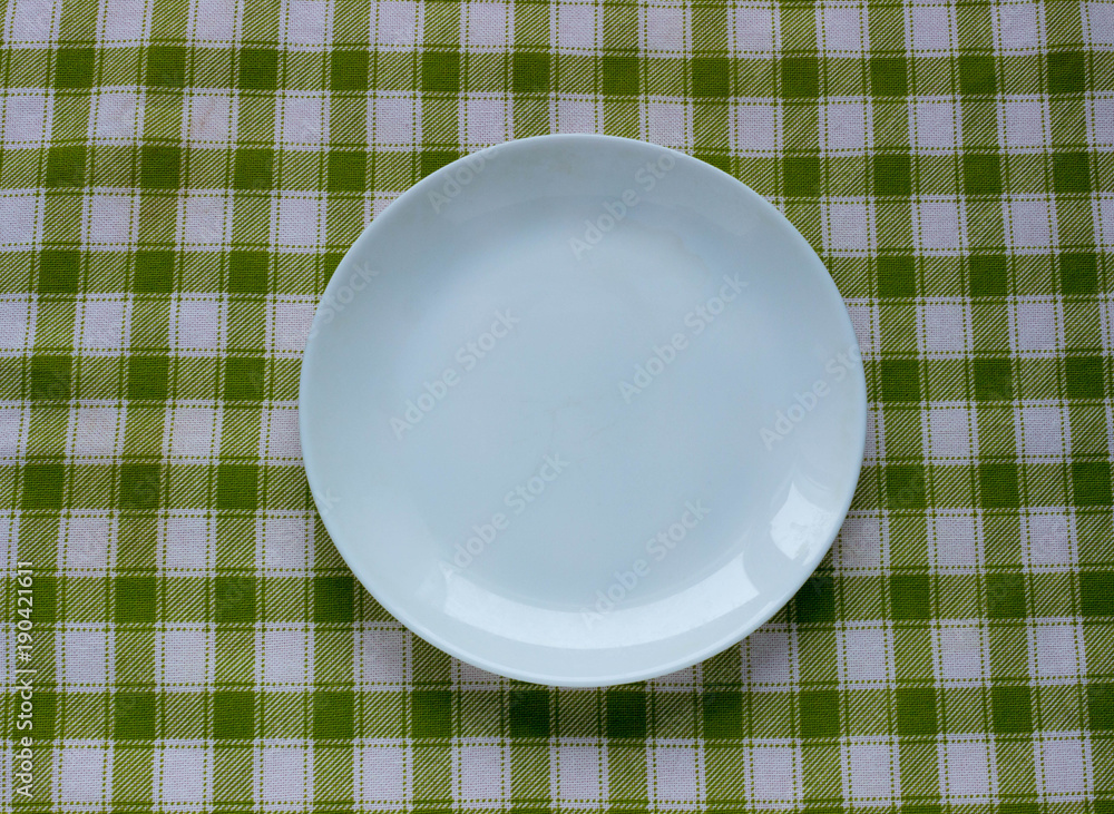 Empty white plate on green checked tablecloth background Empty white plate on green checked tablecloth background