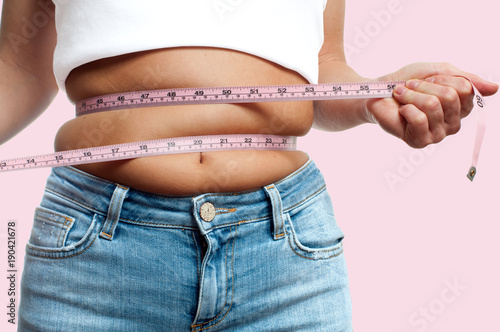 Overweight woman with tape measure around waist on pastel background