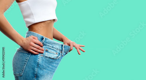 Weight loss. Woman in oversize jeans on green background