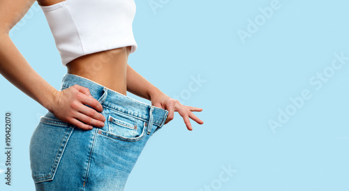 Weight loss. Woman in oversize jeans on pastel blue background photo