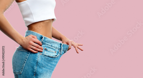 Weight loss. Woman in oversize jeans on pastel pink background