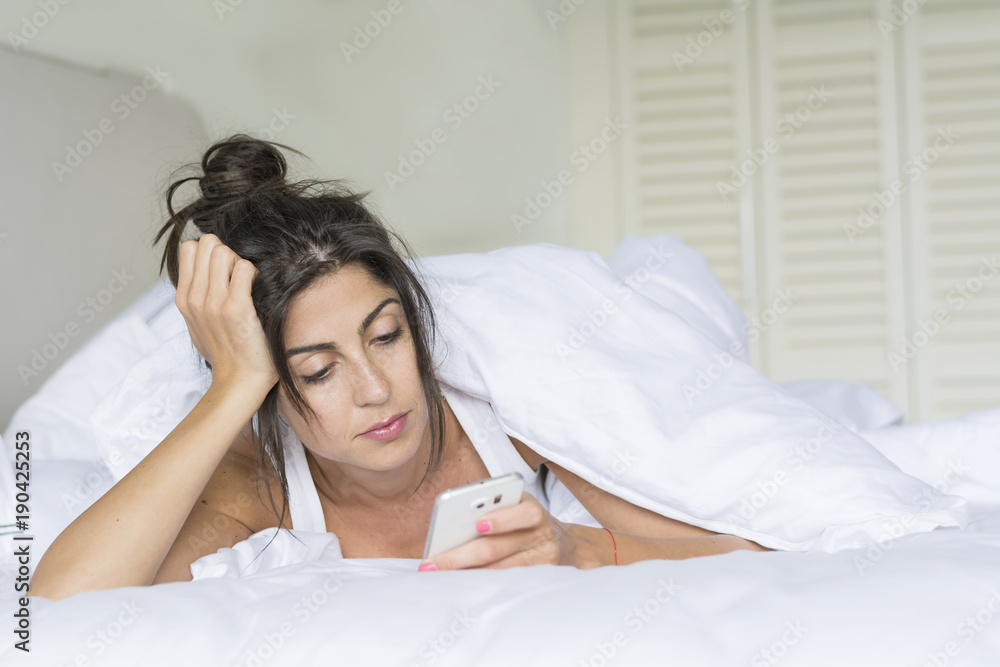 Fototapeta premium Sad Woman Sending Message on the Phone in the Bed