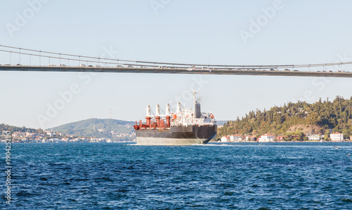Large cargo ship proceeding along the Bosphorus Channel on the background of the bridge on the background