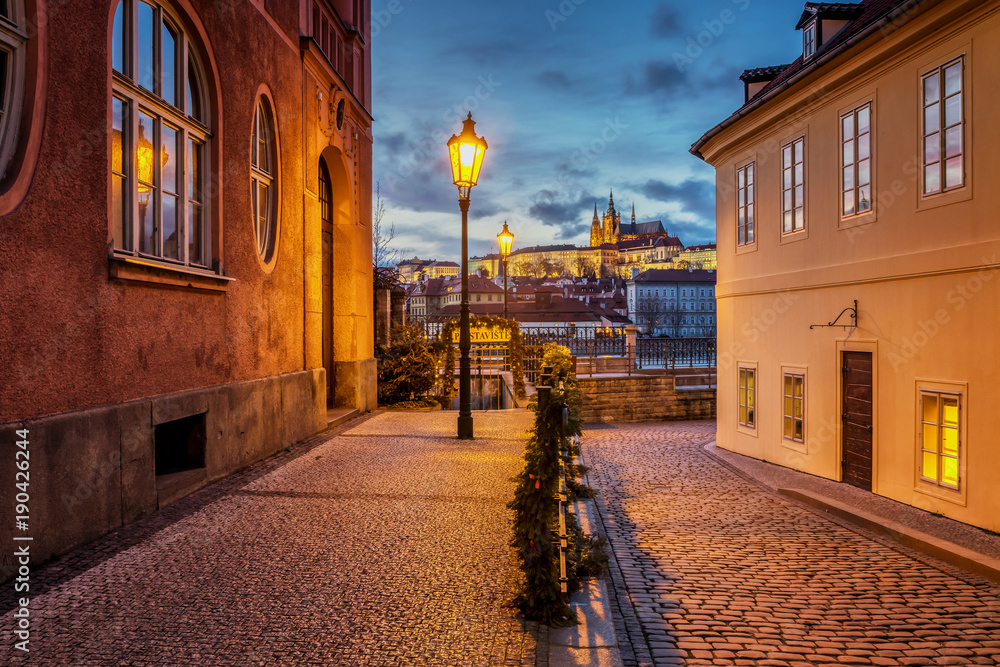 Beautiful view of Prague Castle at sunset from a historical street with gas lamps over the river Vltava.