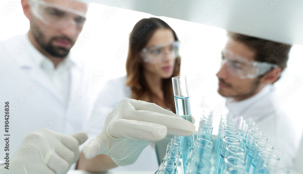 background image is a group of scientists studying the liquid in the glass tube. background image is a group of scientists studying the liquid in the glass tube.