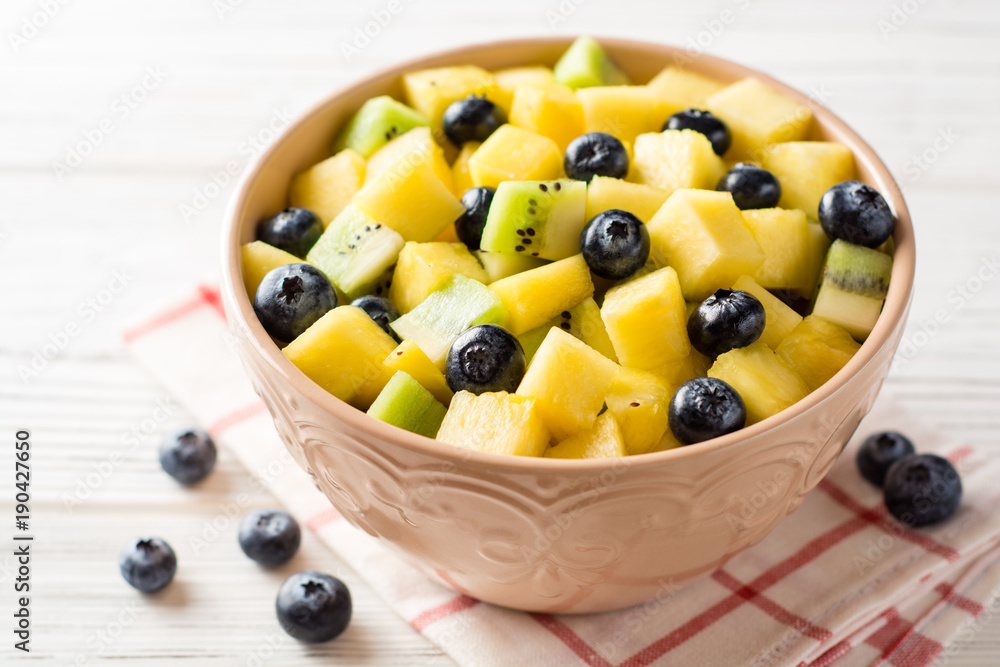 Fresh fruit salad with pineapple, mango, kiwi and blueberries on white wooden background. Fresh fruit salad with pineapple, mango, kiwi and blueberries on white wooden background.
