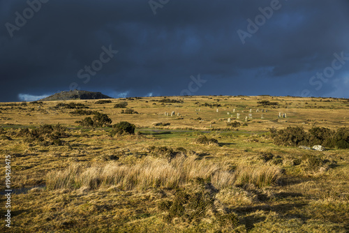 The Hurlers on Bodmin Moor lit with the Golden hour light with Stowes hill in background and moody looking hail clouds on the horizon