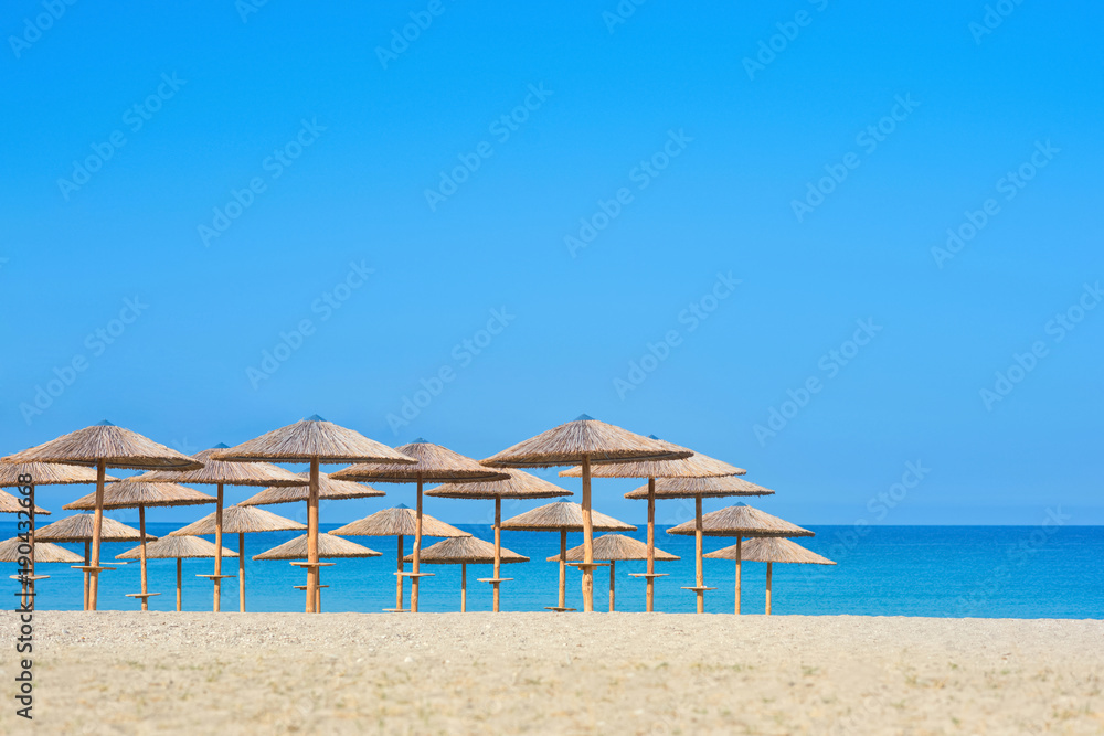 View of tropical beach with big straw umbrellas and sun loungers on the sunset sea background