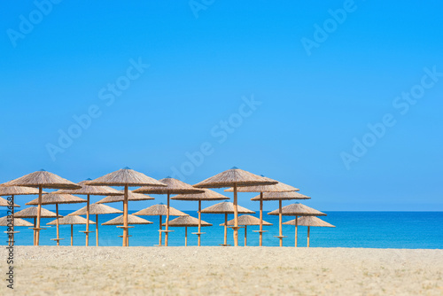 View of tropical beach with big straw umbrellas and sun loungers on the sunset sea background © flowertiare