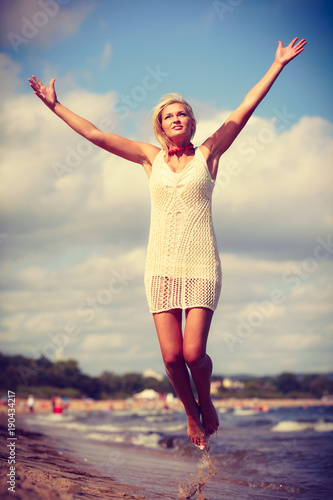 Blonde woman wearing dress playing jumping on beach © Voyagerix