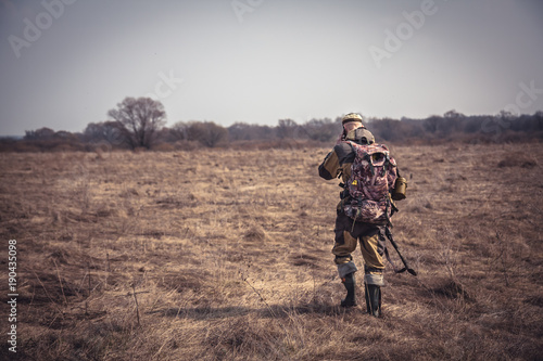 Hunter man in camouflage with shotgun going through rural field during hunting