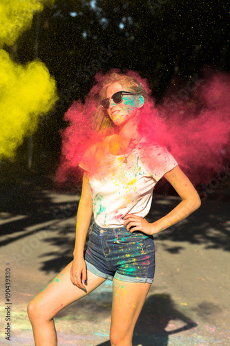 Pleased young woman celebrating Holi festival with pink and yellow dry paint