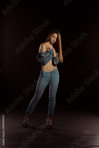 Slim young woman in trendy jeans apparel posing in the dark