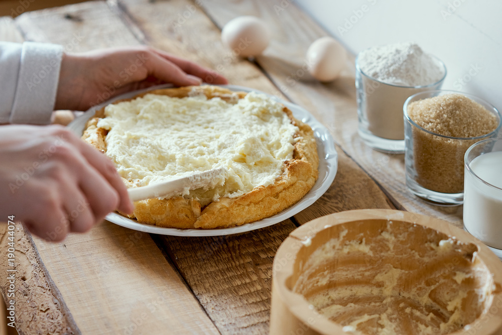 woman puts a cream on the cake on an old wooden table woman puts a cream on the cake on an old wooden table