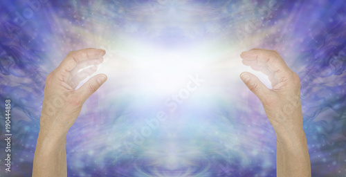 Sending pure unconditional love healing energy - female hands opposite each other with a bright white light beam between against a shimmering blue sparkle background 
