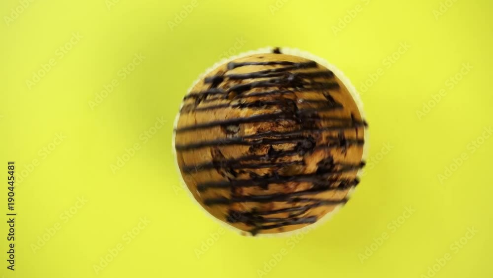 Baking, cake, fresh brown muffin rotates on a wooden background of yellow color. The dessert is spinning fast. It is poured with chocolate. Great for advertising design. Baking, cake, fresh brown muffin rotates on a wooden background of yellow color. The dessert is spinning fast. It is poured with chocolate. Great for advertising design.