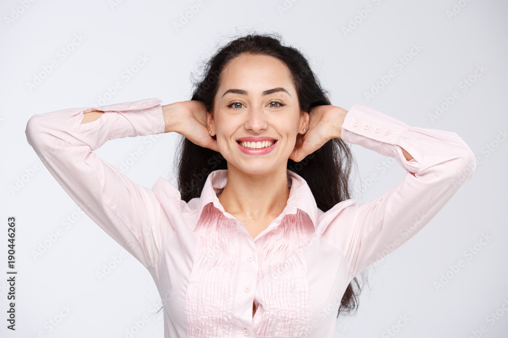 Close-up portrait of a young very beautiful woman with a charming toothy smile, black hair and brown eyes on a white background in a pink shirt. Hands near the head. Positive and joyful emotions