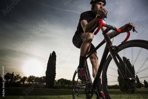 Fototapeta samoprzylepna rowerzysta jedzie o zachodzie słońca na trawie
