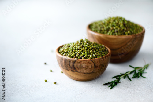 Mung bean, green vigna radiata in wooden bowl and rosemary on grey background. Copy space