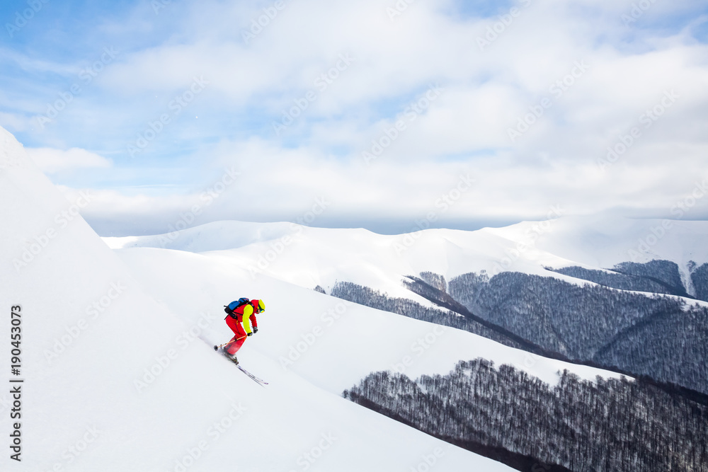 A man is skiing on the slope, wearing brigh  red yellow jumpsuit.