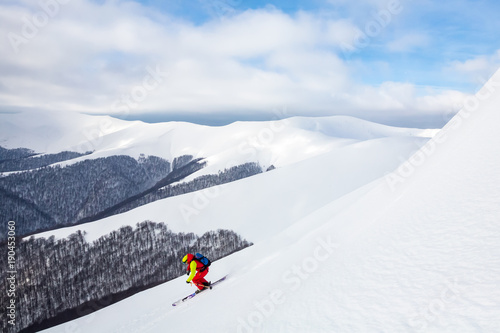A man is skiing on the slope, wearing brigh red yellow jumpsuit.