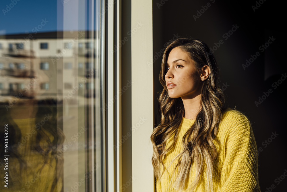 Thoughtful woman looking through window while standing in darkroom at home Thoughtful woman looking through window while standing in darkroom at home