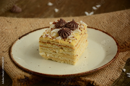 Piece of cake napoleon on a plate with chocolate candys, custard and coconut chips 