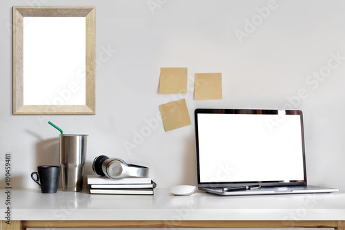 Mockup image of laptop with blank white screen and poster on white wooden table in home studio.