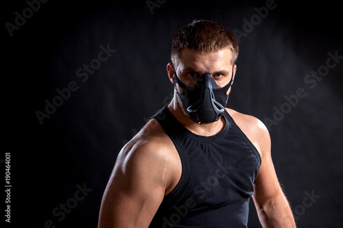Portrait of a dark-haired man athlete in a black training mask, a sports shirt on a black isolated background