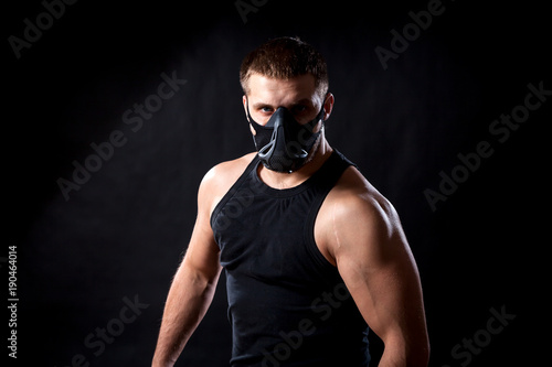 Portrait of a dark-haired man athlete in a black training mask, a sports shirt on a black isolated background