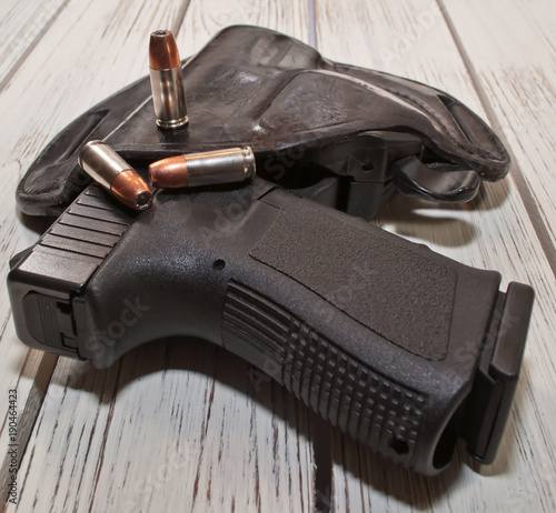 A black 9mm pistol in a holster on a wooden table, three hollow point bullets are on the top of the holster