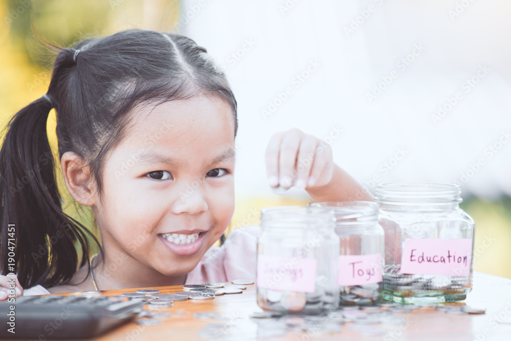 Cute asian little child girl putting coin into glass bottle in the garden. Kid saving money for the future concept Cute asian little child girl putting coin into glass bottle in the garden. Kid saving money for the future concept
