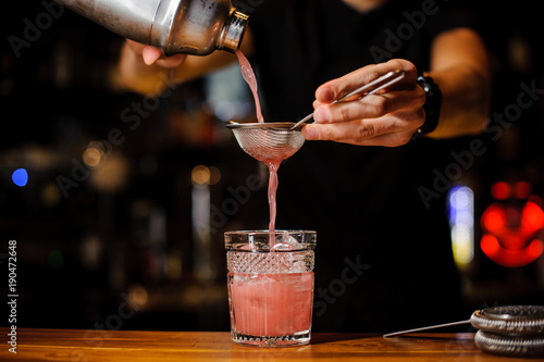 Foto barman poured an alcoholic cocktail from the shaker into a crystal glass